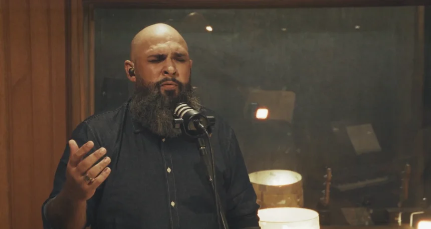 Vitor Teixeira canta de olhos fechados diante do microfone, com uma das mãos aberta.